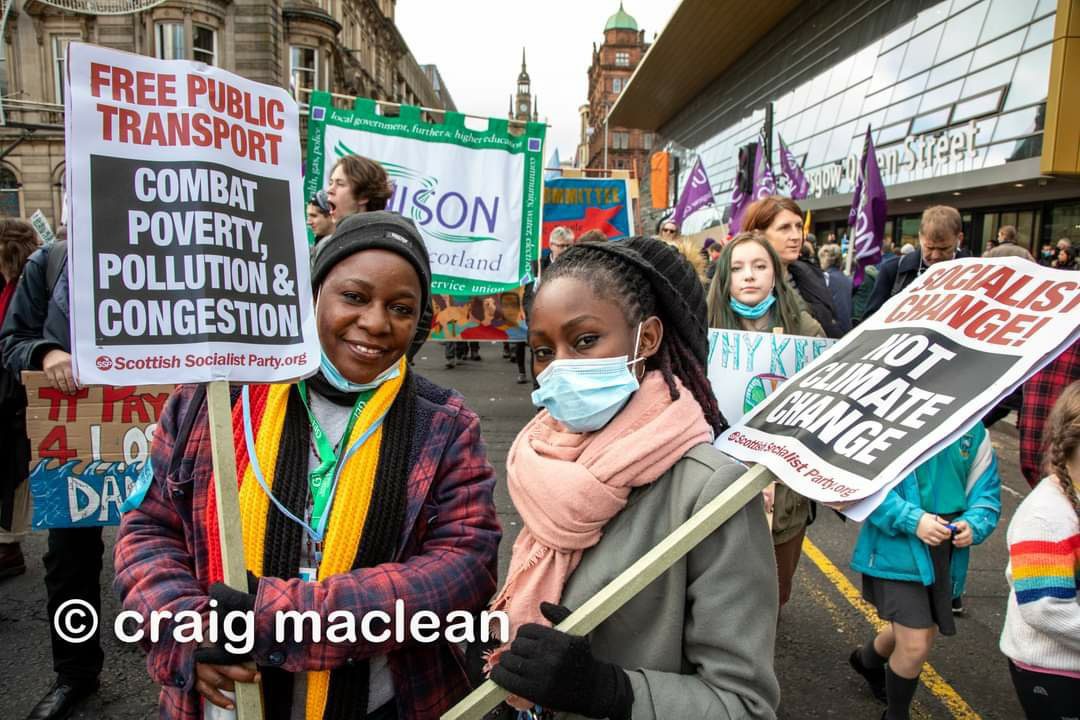 Two women at COP26 march in Glasgow with SSP placards calling for "free public transport" and "socialist change, not climate change".