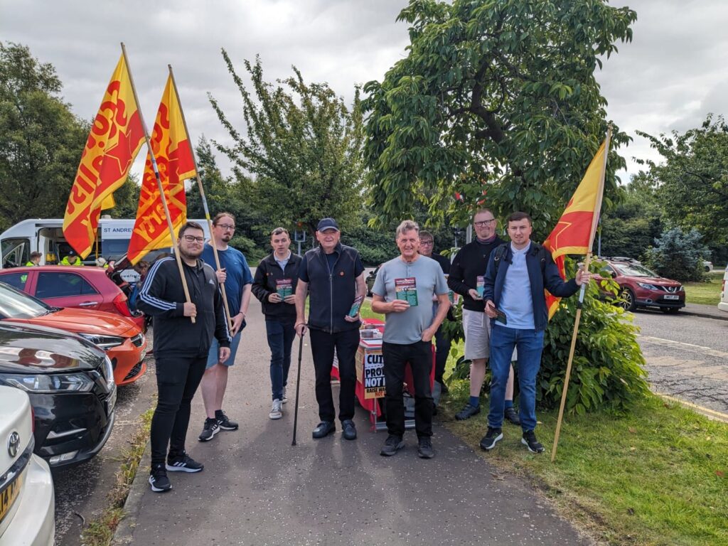 Members of the Scottish Socialist Party rally in solidarity with workers at Grangemouth. They are holding yellow and red flags on wooden flagpoles.